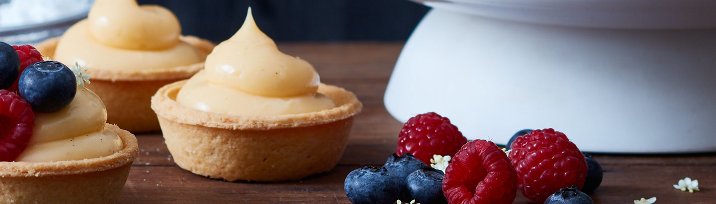 A picture of a selection of custard filled tarts, served with raspberries and blueberries. 